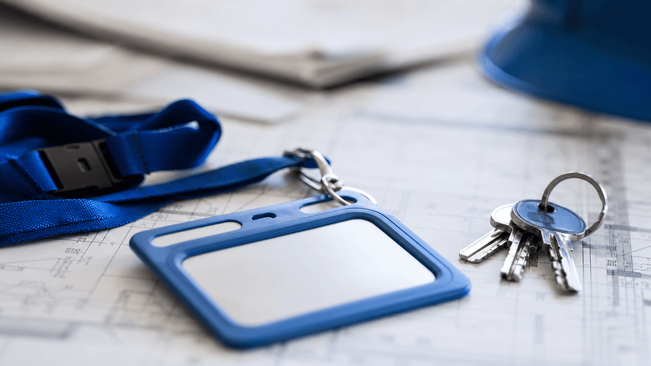Porte-badge, trousseau de clés et casque de chantier posés sur des plans techniques